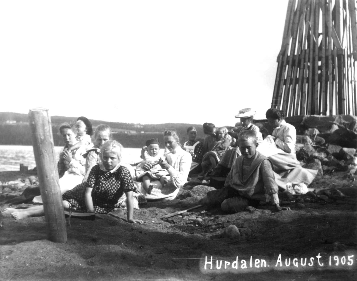 Friluftsliv, persongruppe samlet utendørs, Hurdal, Akershus, august 1905. I bakgrunnen nedre del av en vindmølle som sto på neset ved stranden og pumpet vann fra sjøen til hagevanning.