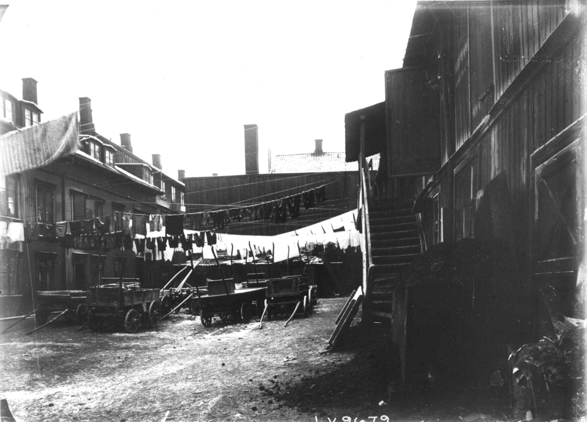 Gårdsplass med boliger, muligens på Rodeløkka, Oslo. Hestekjøretøyer plassert på plassen med klesvask over.
Fra boliginspektør Nanna Brochs boligundersøkelser i Oslo 1920-årene.