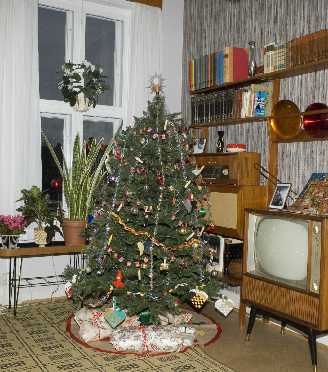 "Teak, TV og tenåringer - 1965". i OBOS-gården, Wessels gate 15. Norsk Folkemuseum, Oslo. Stua med pyntet juletre. Den grå og sorte kurven med rød hank ble laget i 1965.