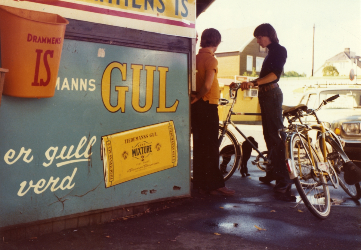 To gutter med sykkel ved siden av kiosk. Skilt med reklame for Tiedemanns Gul.