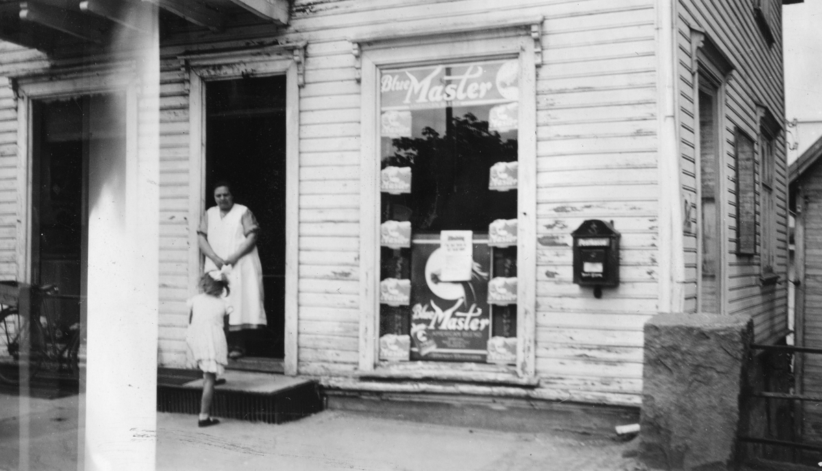 En dame og en jente i døren til forretningen Tom Stallemo i Kristiansand, 1937.