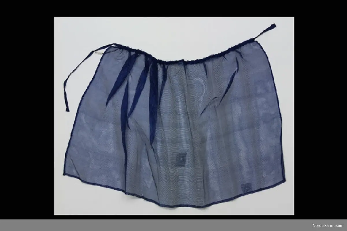 Inventering Sesam 1996-1999:
L 30 cm
Dockförkläde av tunt blått siden, dragsko i midjan med knytband.
Helena Carlsson 1996