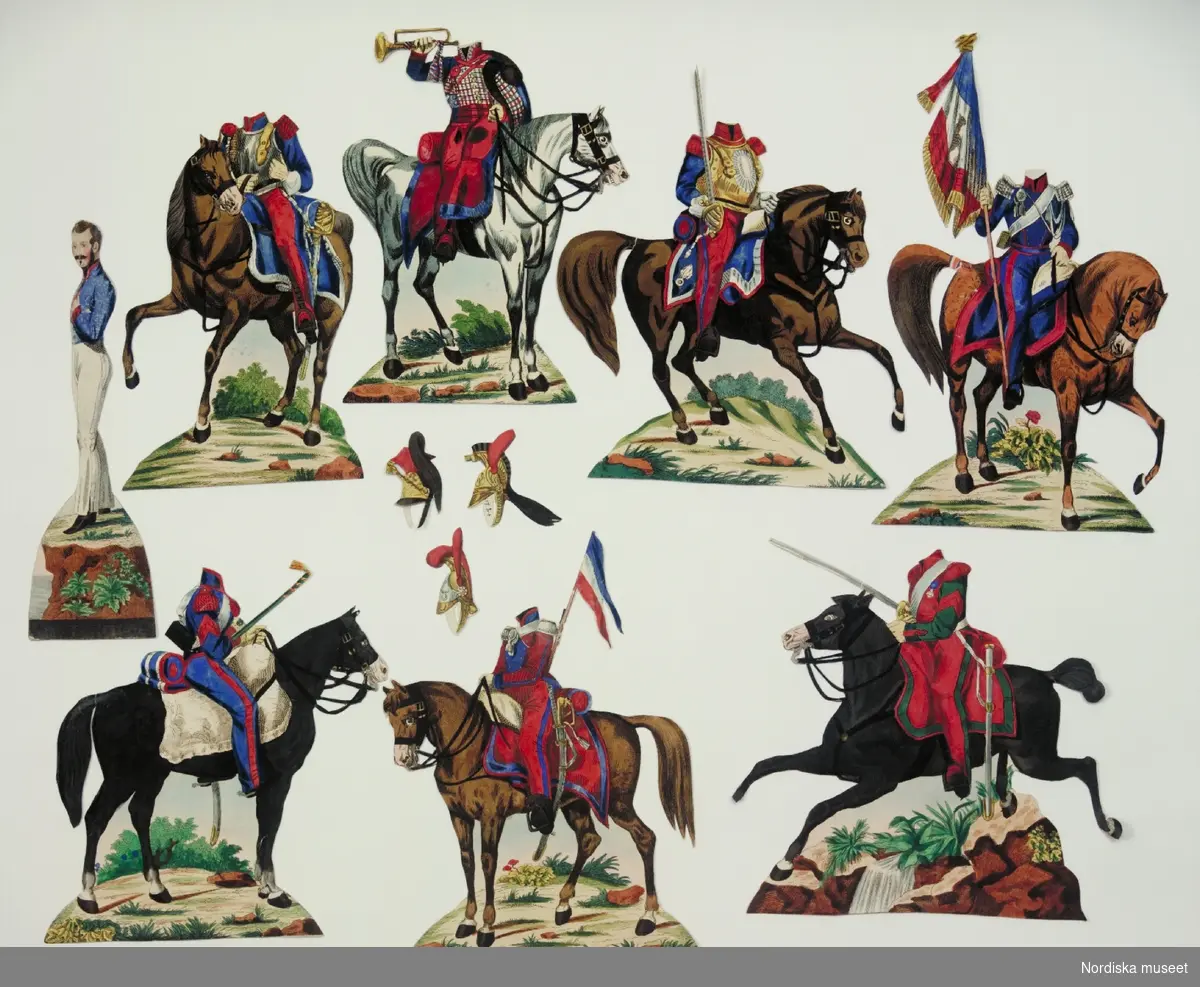 Inventering Sesam 1996-1999:
Kartong H 31  B 22,8 (cm)
Pappersdocka (b+), 11 delar, i originalkartong (a+), svart tryck, handkolorerad, förest. man iklädd blå uniformsjacka och vita byxor, 7 st tillhörande hästar med uniformerade kavallerister, dubbelsidiga, med öppning, så att figuren kan stickas in samt 3 st lösa kaskar med plymer. Uniformer och fanor målade i rött, blått och vitt. 
Kartong av papp, med lock, motiv av kavallerister och text: "THE HORSE-SOLDIER / (Le) Cavalier   Der Cavallerist". Mönsterpressad guldlist av papper runt lockets ytterkanter.
Anna Womack 1996