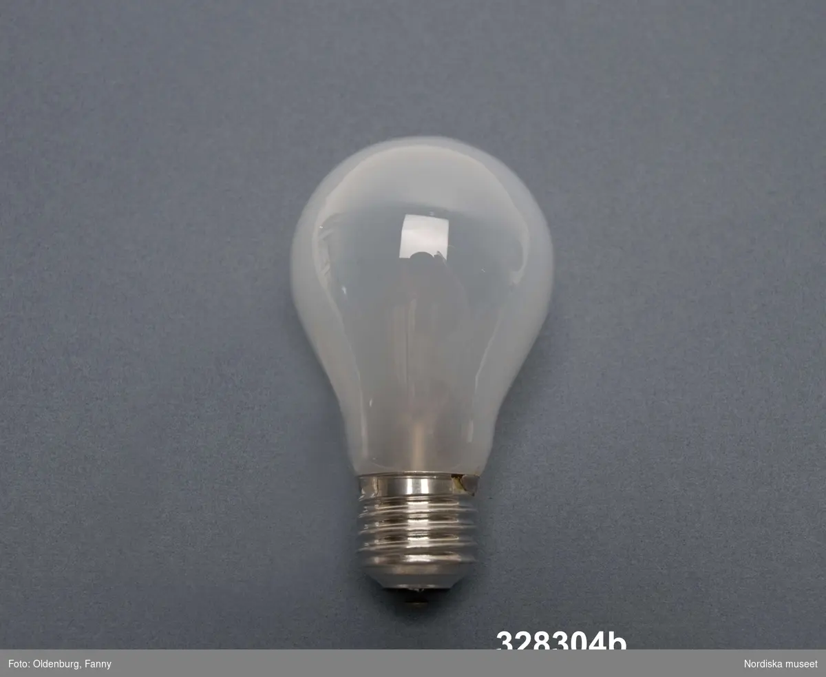 a+ = lampskärm
b = glödlampa 
a+) Taklampa av plast, för elektrisk belysning. Halvklotformad skärm, kupa, av orange plast. Lamphållare av brunt trä håller skärm och vit plastcylinder som inuti skärmen omger glödlampan lodrätt från lamphållaren ned till lampkupans nederkant. Sladd- och takfäste av vit plast, sladden avslutas med kontakt. Klistermärke på takfästets kopp med texten: "MADE IN SWEDEN BY LUXUS VITTSJÖ DES UNO o ÖSTEN KRISTIANSSON". Ingjutet i koppens insida: "LUXUS MADE IN SWEDEN".
b) Glödlampa, vitt halvgenomskinligt glas, päronformad, skruvfäste av vit metall. Text på toppen "PHILIPS CLASSICTONE 60W 230V". Tillverkningsår sannolikt 2004. Längd 10 cm.

Givaren köpte taklampan vid flytt från Malmö till Stora Mossen, Bromma 1959 och har använt den som taklampa över köksbordet fram till 2004.
/Maria Maxén 2006-01-23