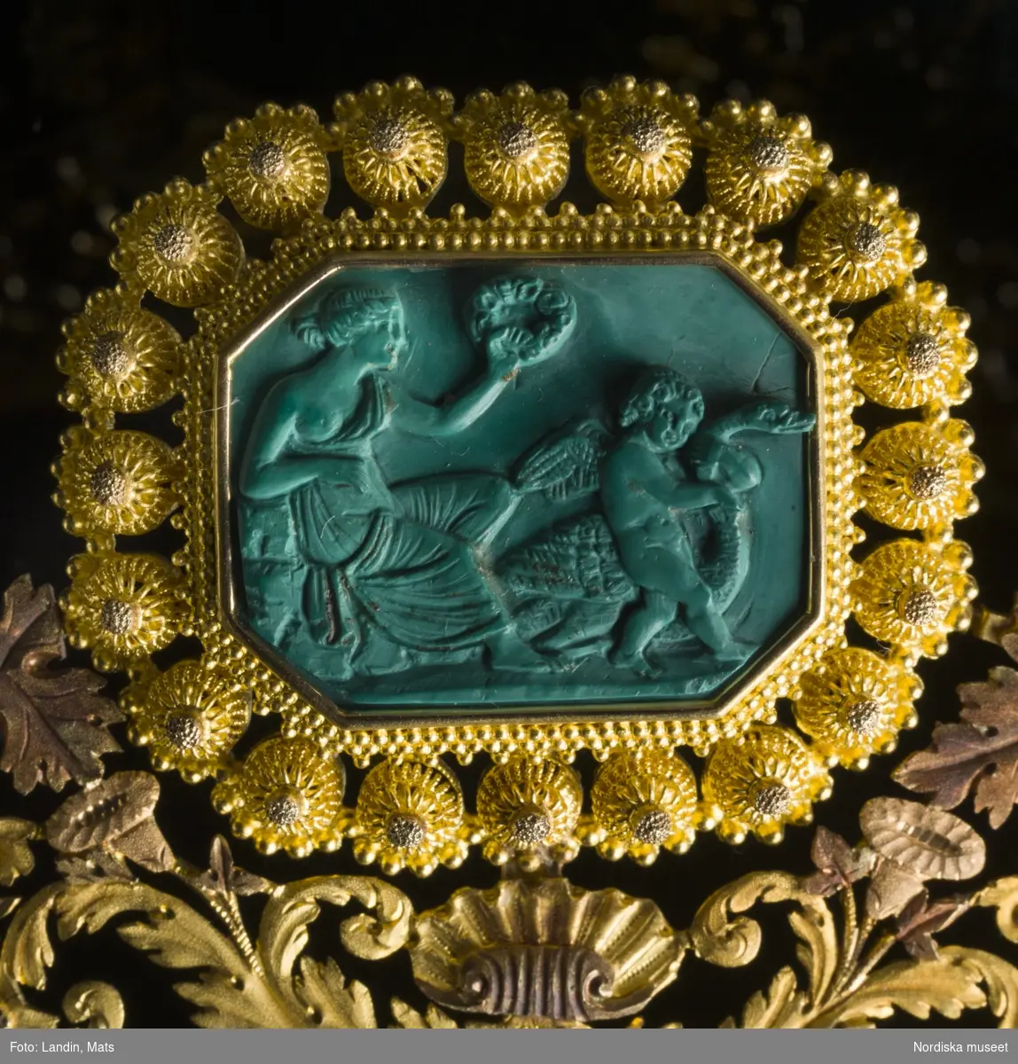 Smycken. Drottning Sofias garnityr utfört av guld och malaktit. Nordiska museets föremål Inv nr 990047.

Garnityret har tillhört Sveriges och Norges drottning Sofia (1836-1913).  Kaméerna är är skulpterade av det ovanliga smyckematerialet malakit, en grön kopparhaltig sten. De antika motiven är inspirerade av den danske skulptören Bertel Thorvaldsens bildvärld. Garnityr var vanliga under 1800-talet och var högsta mode då det användes av drottningen. Garnityret är tillverkat av Simon Petiteau, 

Se även relaterade poster/objekt.