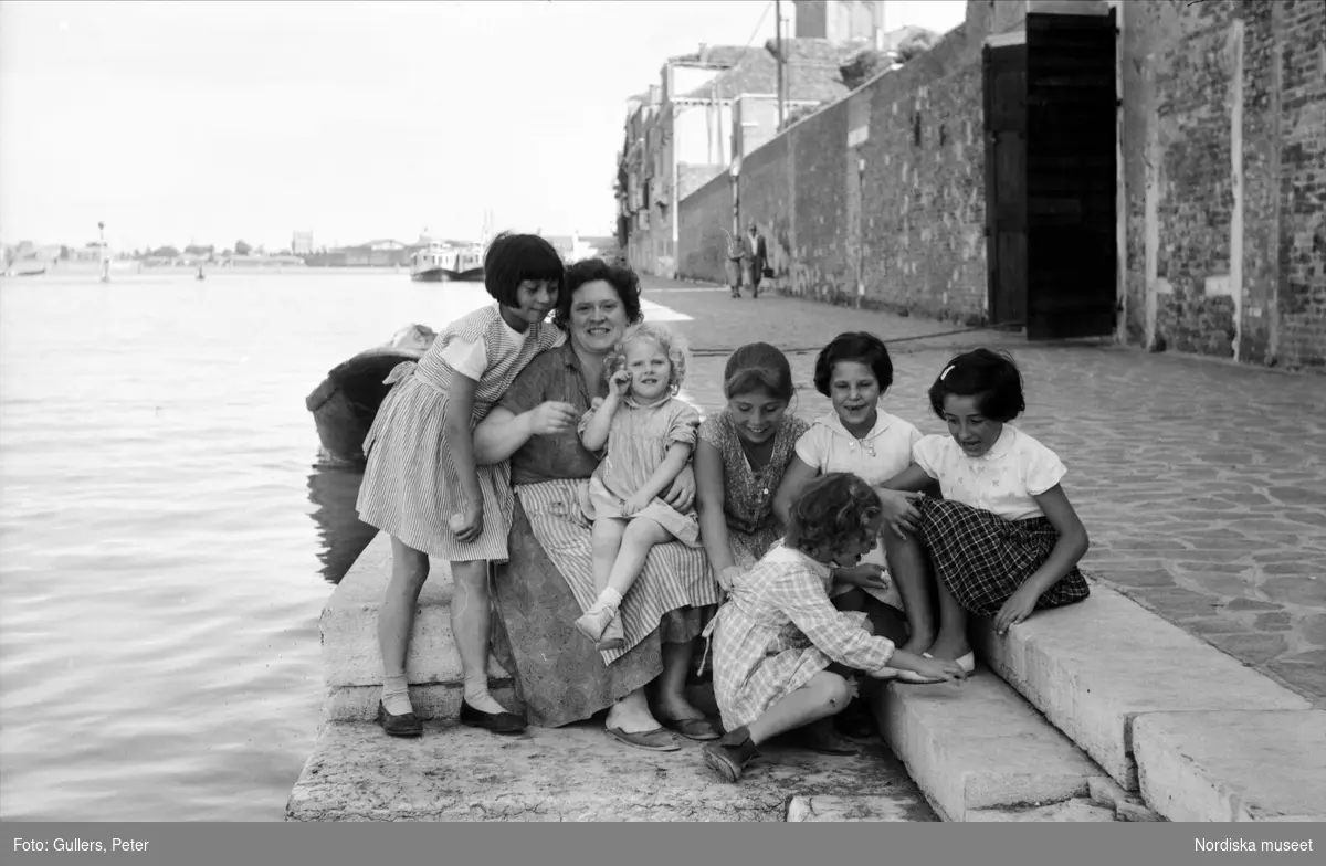 Kvinna och sex flickor sitter på kajen. Neapel, Italien