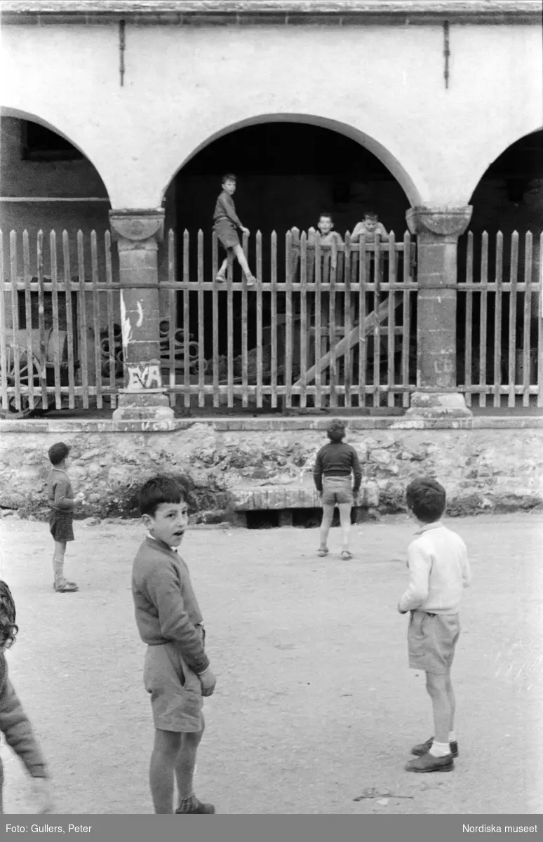 Pojkar leker på gata och klättrar på staket. Levanto, Italien