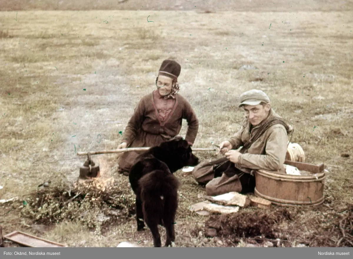 Påskrift på monteringen: "Rast under flyttningen." Samiskt par kokar kaffe, hund i förgrunden. Jokkmokk, 2 juli 1947.