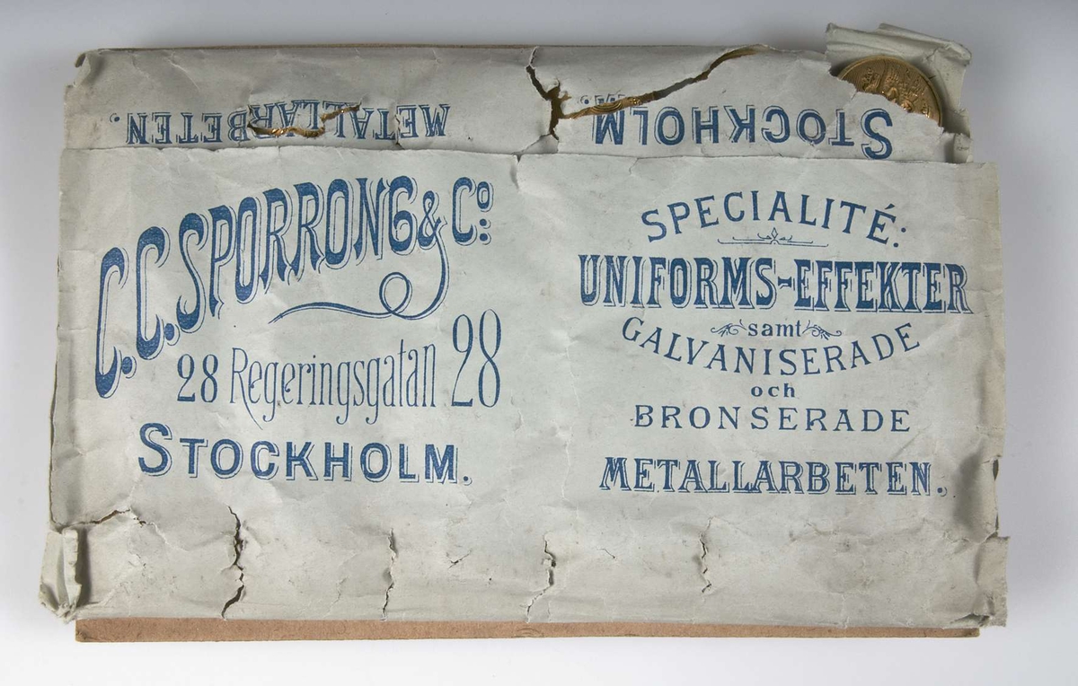 Tolv knappar av förgylld mässing till järnvägsuniformer, fästade på  pappskiva med etikett av ljusblått papper med mörkblå text: C.C.Sporrong & Co. Regeringsgatan 28, Stockholm.
