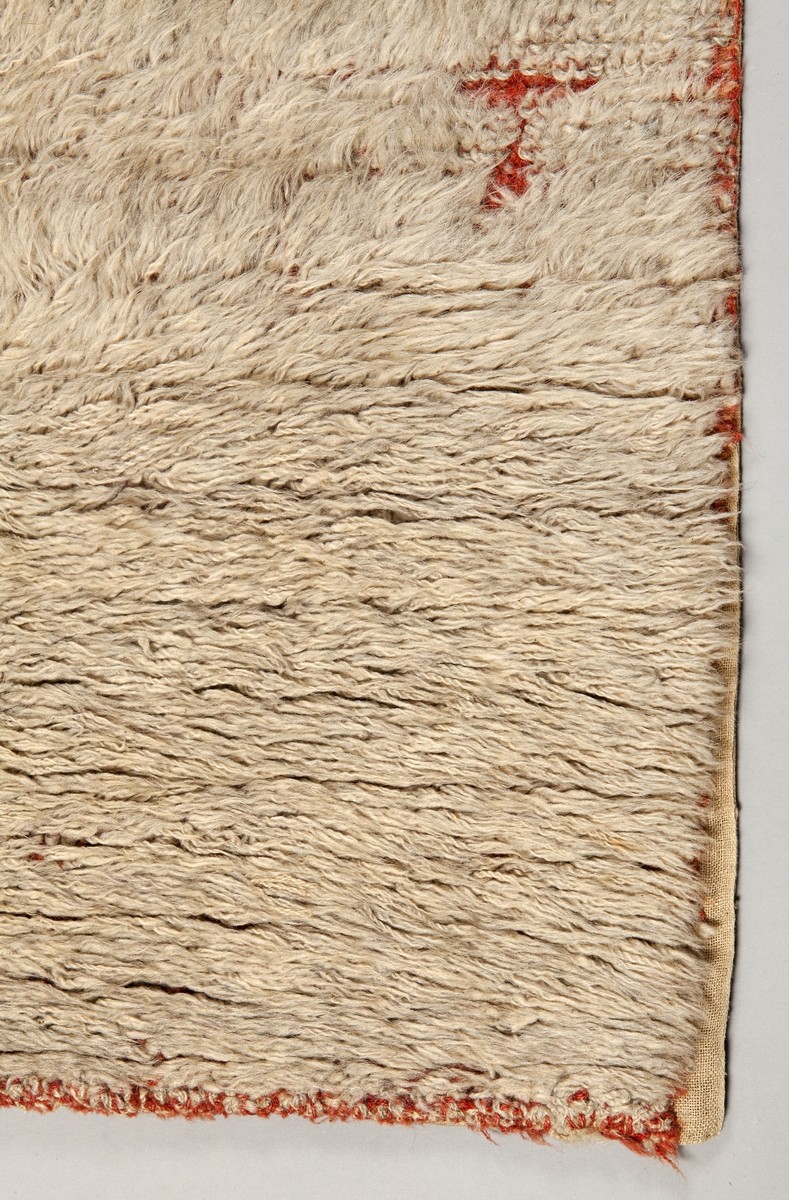 Slitrya vävd i två våder hopsydda med söm mot flossan. Bottenbindning i korndräll mönstrat i olika breda röda och beiga vertikala ränder. Varp av s-tvinnat beigt och rött ullgarn, 13 varptr/cm och inslag av s-tvinnat rött ullgarn, 9 inslag/cm. Täta nockor av z-tvinnat glansigt naturgråvitt ullgarn, knutna med giordesknutar över 4 varptrådar, med 4 varptrådar emellan nockorna och 4 inslag mellan nockraderna. 16 knutar/10 cm 9 knutrader/10 cm. Nockorna vända åt olika håll på våderna, ena halvan ljusare. I nederkanten av ena våden är en bit iskarvad. Nockorna syns ej från slätsidan.
Mönster: naturgråvit med bård av röda viggar i överkanten. På baksidan broderat med kedjestygn: Anno 1773 med vitt garn. Breda band och lappar av stödtyg på baksidan. Upphängningssko.