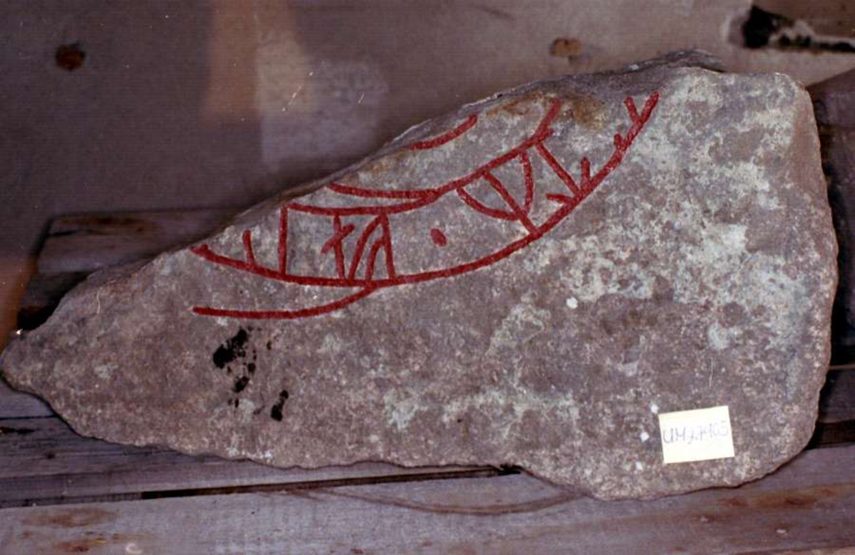 Fragment av runsten av spräcklig, rödaktig granit med grå inslag i  ristningsytan. Runhöjd 5,5 cm. Inskrift: = " ....efter fader...."