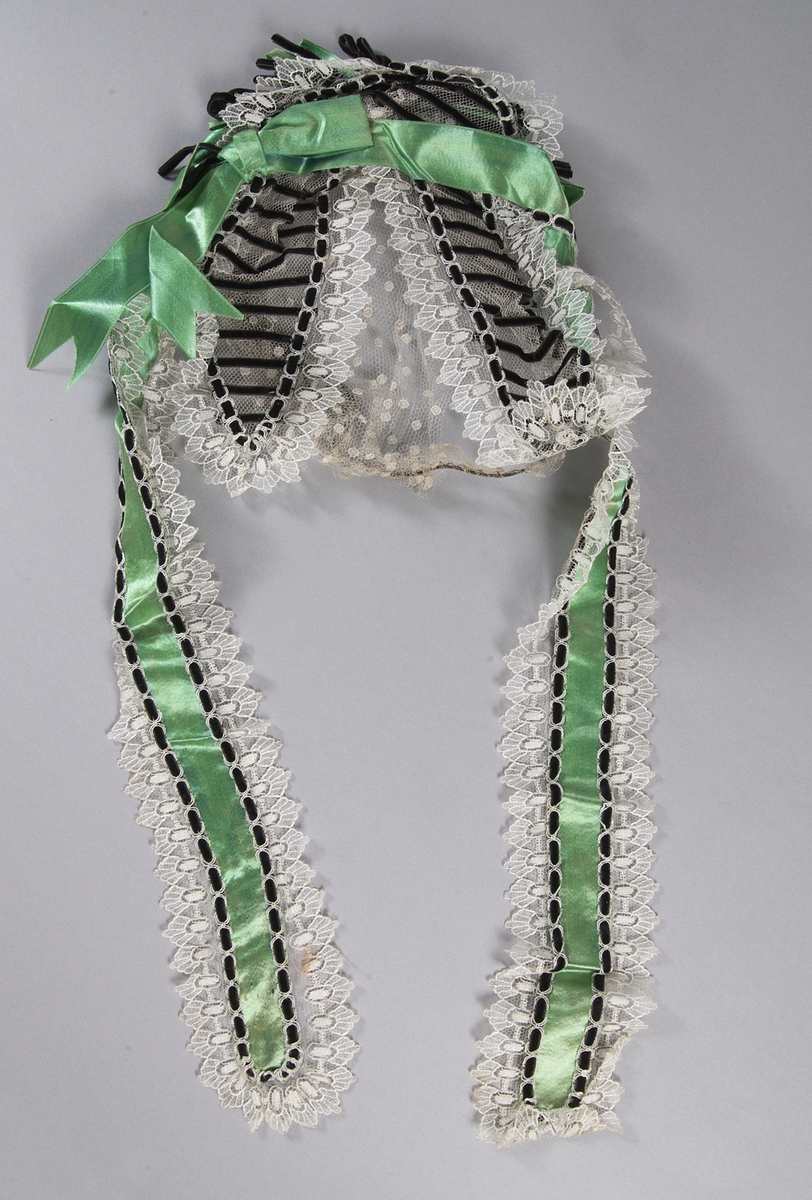 Hårklädsel 1800-1900-tal. Vit spets med band och rosetter i grönt siden och svart sammet.