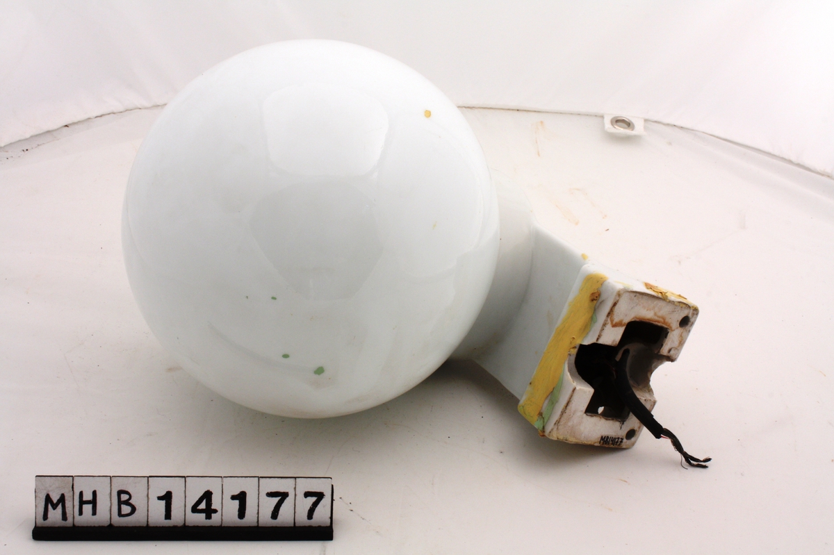 Vegglampe med hvit glasskuppel som er kuleformet. Kuppelen er festet til en sokkel i steingods som ender i veggfeste. En ledning stikker ut av enden på sokkelen.