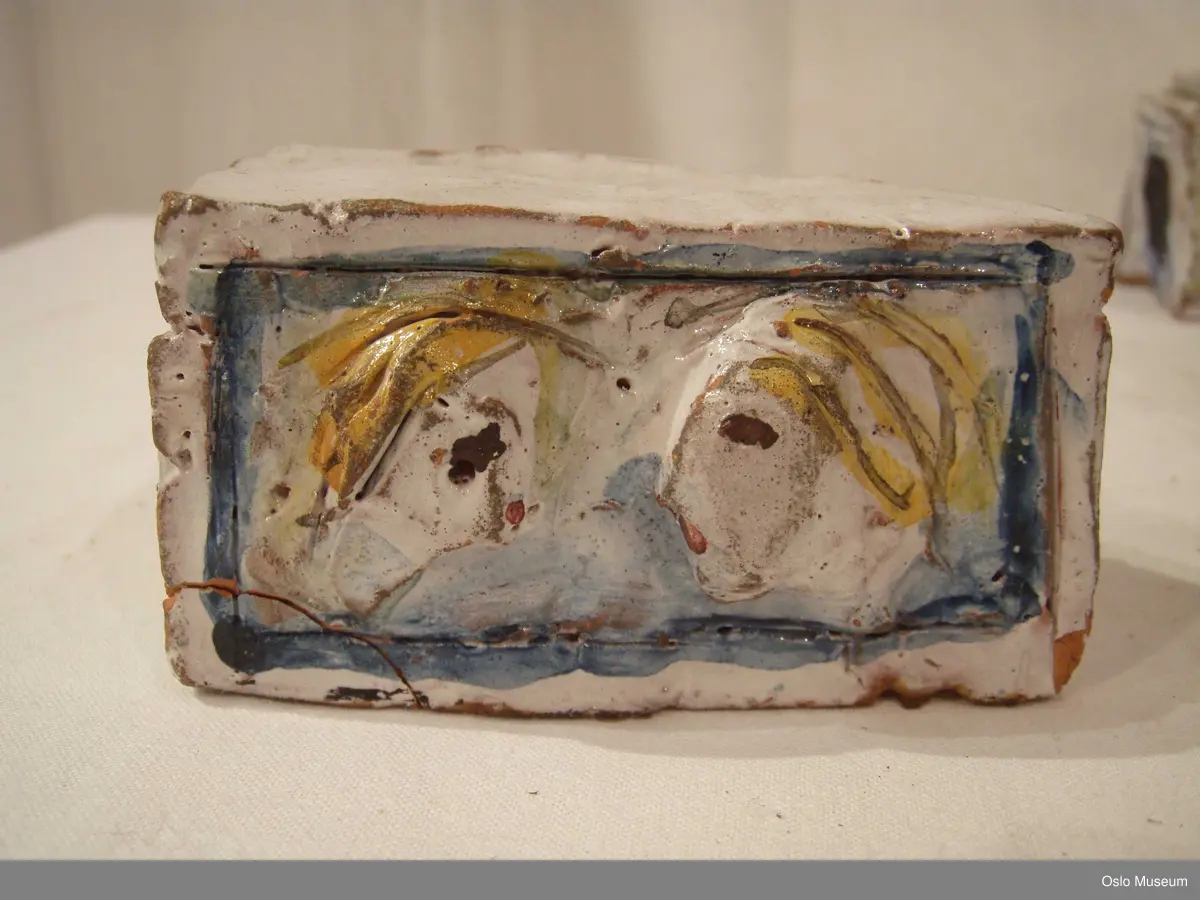 Scenografimodell av keramikk. Glasert i hvit bunnfarge med dekor/detaljer i blått og gult. 7 deler. Spesiallaget oppbevaringseske.