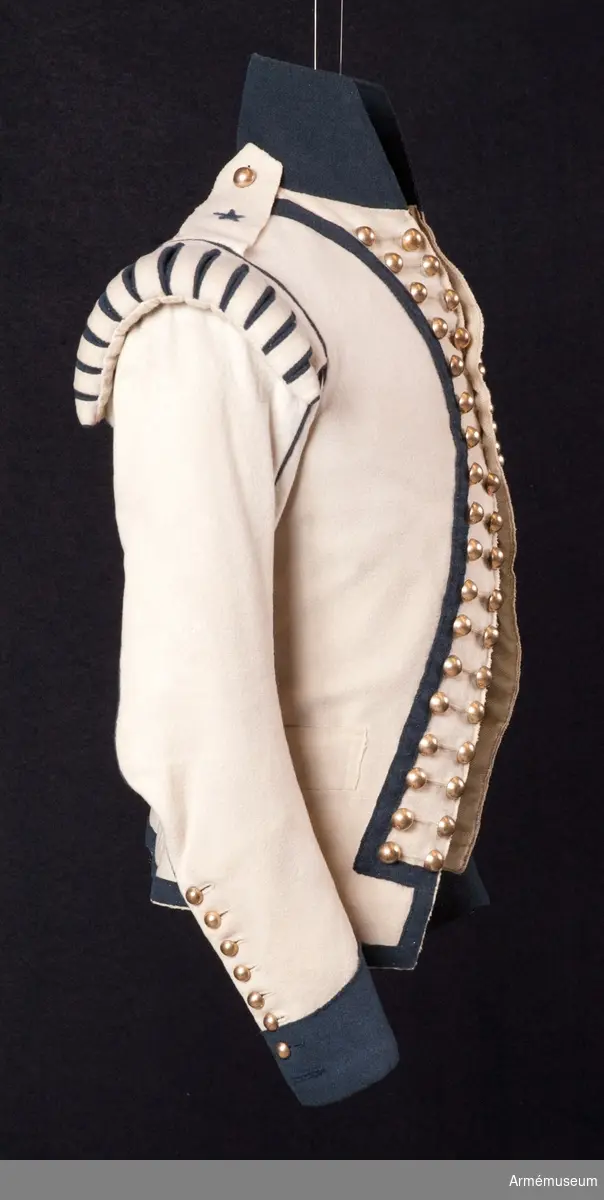 Jacka m/1792, av vitt kläde med hög krage, passpoaler, ärmuppslag och andra detaljer i mörkblått kläde.
Plagget är kraftigt svängt mitt fram, knäppt med tre knapprader med 18 guldfärgade klotknappar i varje rad, varav bara de 3 på mitten går att knäppa. Övriga knapphål är stumma.
Vid axeln finns stoppade axelkarmar av vitt kläde med slitsar fodrade med blått kläde. Här finns även fastsydda axelklaffar av enkelt vitt kläde med en blå stjärna applicerad. Axelklaffarna fästs ner med en enkel klotknapp av samma typ som övriga.
Ärmarna är tvåsömsärmar med blå passpoaler i båda sömmarna och sprund längst ner på ärmen som knäpps med 8 mindre kulknappar i varje. I höger ärm saknas en knapp längst ner.
Två grunda horisontella fickor. Litet skört bak.
Jackan är fodrad med fint kypertvävt ylletyg i bålen, men med tuskaftvävt linne- eller hampatyg i ärmarna.

Grupp C I.