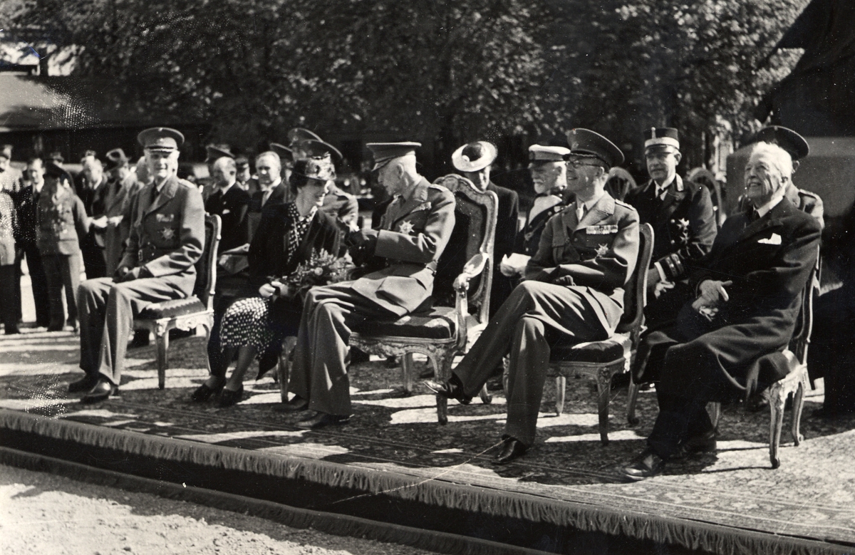 Kung Gustaf V, prins Gustaf (VI) Adolf, prinsessan Sibylla och prins Eugen och flera officerare sitter på podium och betraktar uppvisning(?).