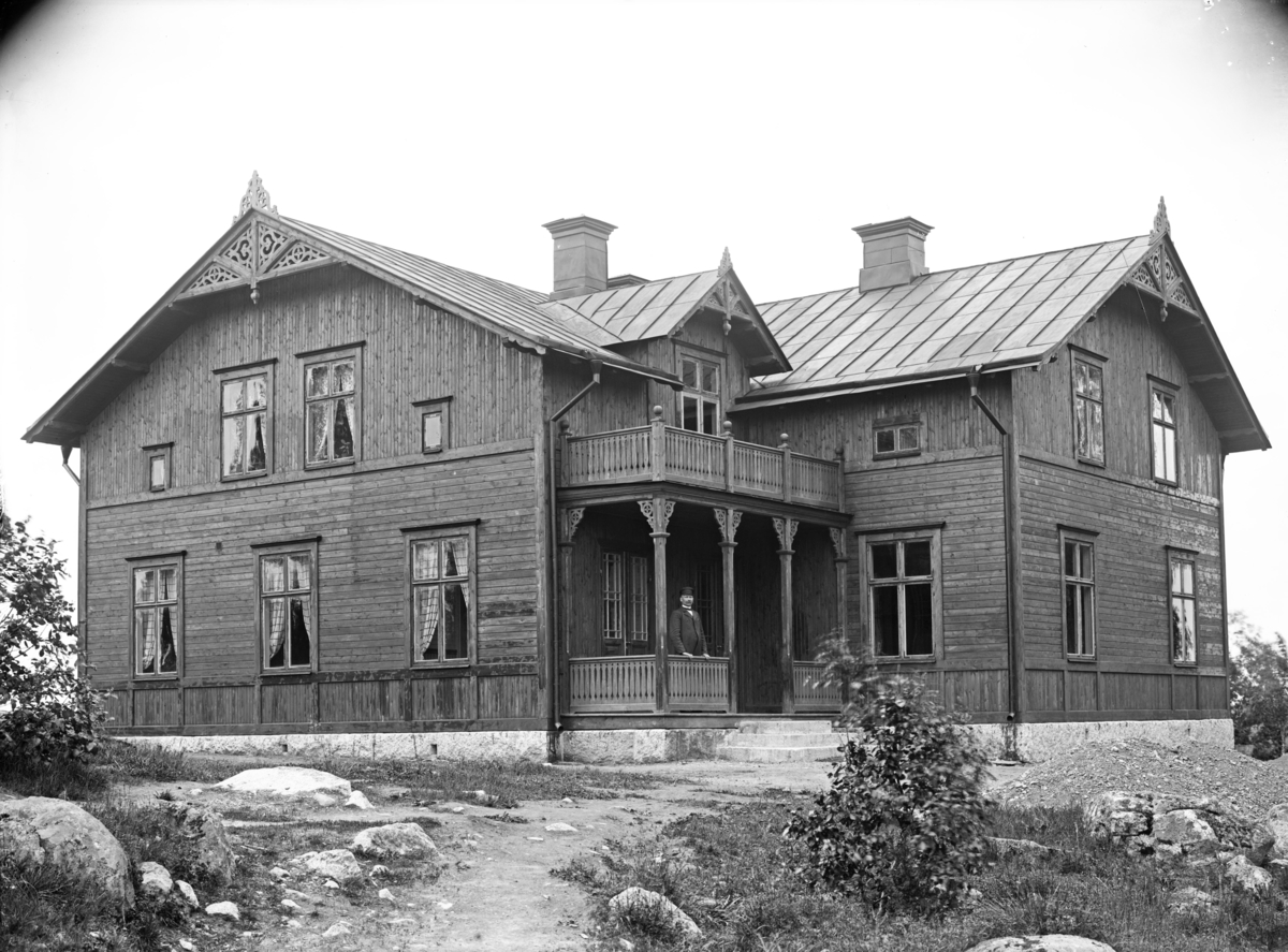 Man på veranda till stor byggnad, oidentifierad, troligen 5 juni 1906