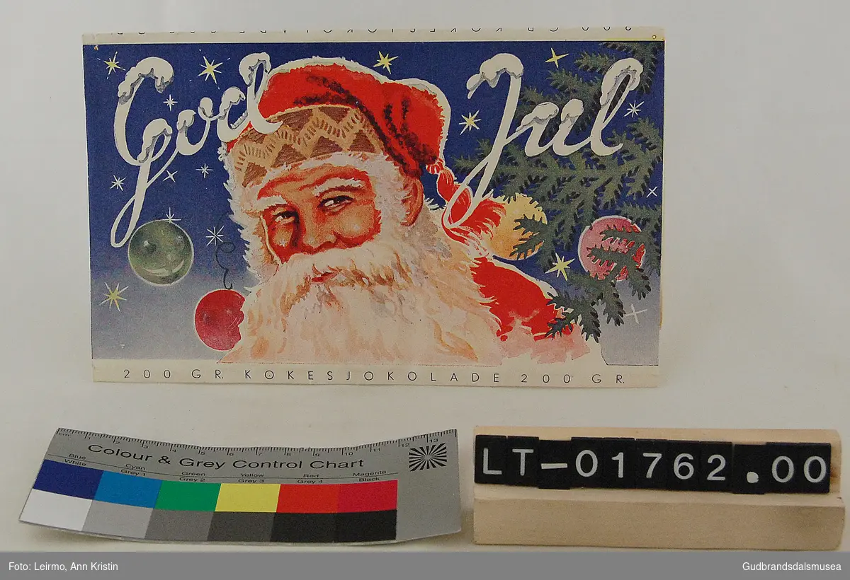 Papiremballasje, har vært rundt en kokesjokoladeplate. Dekorert med julemotiv, julenisse og påskriften God Jul. 
I følge giver fra julen 1939.