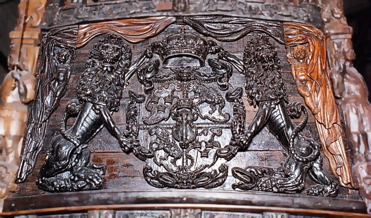 Skulpterad sköld med upprätt, mot höger gående lejon. Lejonet är snidat i hög relief, med heraldiskt stiliserad hållning. Sköldens kontur är rokokomässig, med kanter av varierande bredd och rik pärlbroskdekoration. Upptill avslutas skölden med en ellipsformad broskvolut. Sköldens baksida är slät.

Text in English: Shield with upright, rightward-facing lion. The lion is carved in high relief and reproduced in perspective. It is seen in profile, and its posture is heraldically stylised. The shield has an almost rococo-like outline, with edges of varying width and rich earshell work decorations.The top is finished with an ellipse-shaped pearlwork scroll. The reverse side of the shield is smooth.