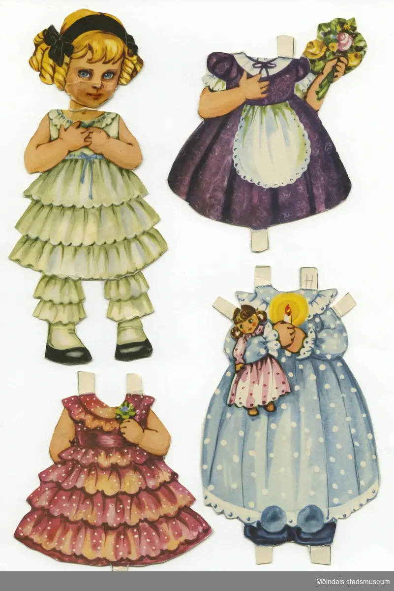 Pappdocka med kläder från 1950-talet. Docka och kläder är märkta "Henriette" på baksidan - dockans namn. Dockan föreställer en liten flicka med blont hår och hårband, iklädd underklänning och mamelucker med volanger, samt skor med vita damasker. Garderoben består av tolv klänningar och en nattsärk i 1800-talsstil. Docka och kläder förvaras ihop med annan docka (MM 04669), i ett brunt kuvert, märkt med blyerts "4 år Annika", men är ursprungligen från "KF Konsum - hushållens förening för lägre levnadskostnader". 