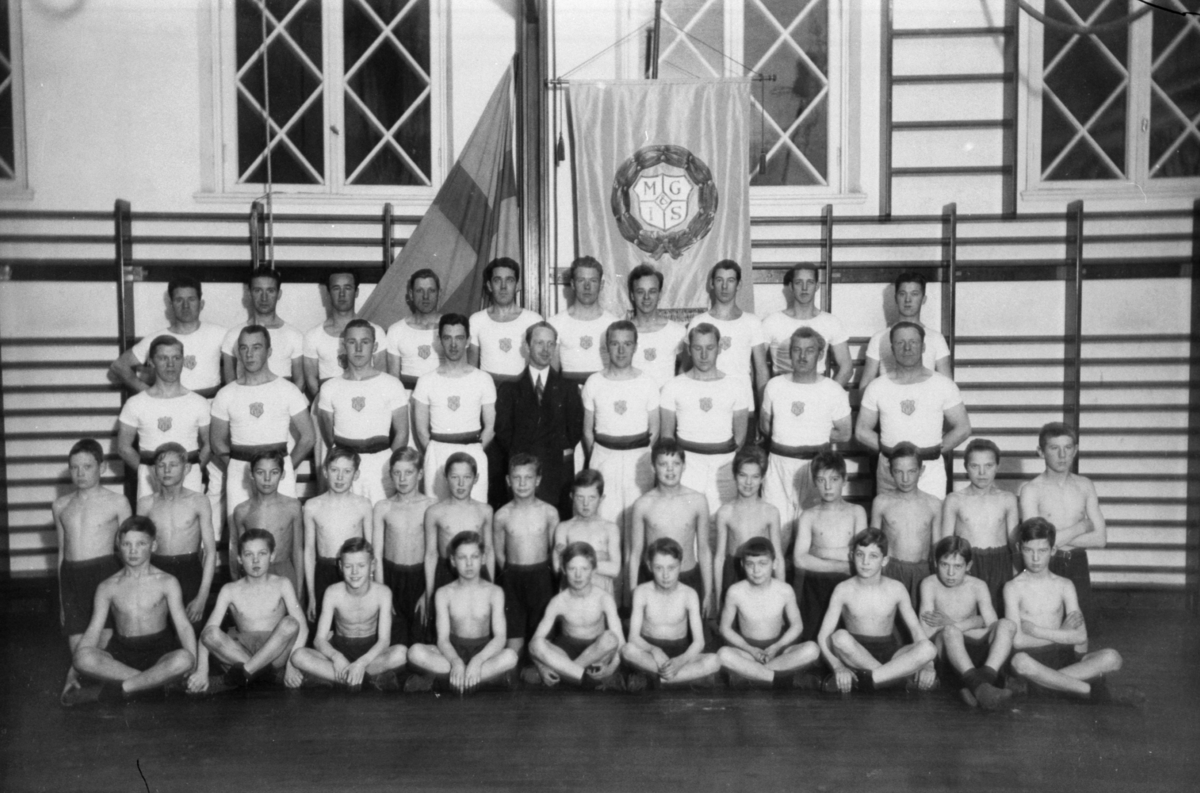 Mölndals gymnastik och idrottssällskap uppställda i Centralskolans gymnastiksal framför standar MGIS.
Kvarnbyskolan kallades vid den här tiden för Centralskolan.