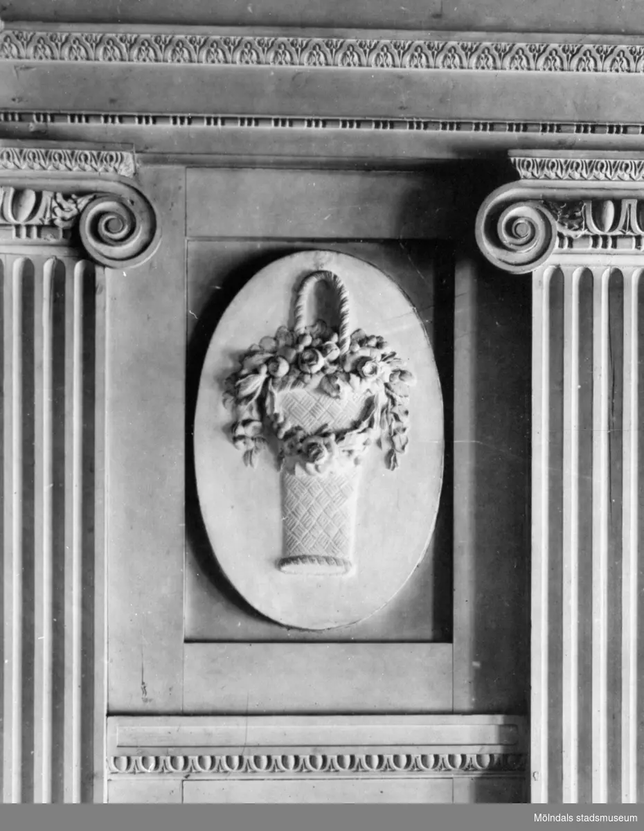 I en tablett, en stående oval relief med emblemet "blomsterkorg", placerad ovanför årstids-gipsfiguren "Våren" av Gioacchino Frulli (1766-1801). Denna sitter på nordöstra väggen i stora salongen på Gunnebo slott.