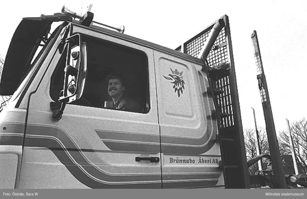 En chaufför sitter i en lastbil märkt "Brännabo Åkeri AB", 1980-tal.
Bilden ingår i serie från produktion och interiör på pappersindustrin Papyrus.
