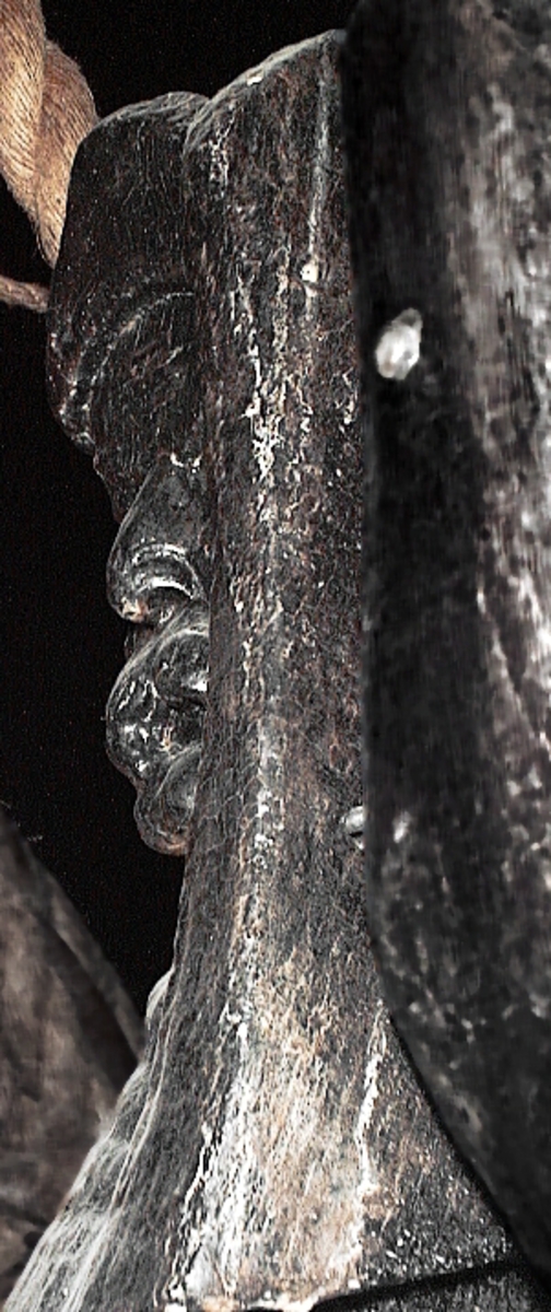 Skulptur av en triton, svängd mot vänster.
Figuren är framställd i högerprofil och avtecknar sig i hög relief mot  bakstycket. Tritonen har ett kraftigt ansikte, böjd näsa och treflikig mustasch. På huvudet sitter en bladsmyckad hjälm. Armarna är ersatta av långa, flikiga bladslingor. Bålens övergång i den fjällförsedda fiskstjärten markeras av stora bladbildningar. Stjärten döljs till största delen av den under liggande drakens ringlande stjärt och vinge, se fyndnummer 05967. På baksidan finns urtag för relingslisten.
Skulpturen är välbevarad.
Text i fyndliggaren:
Tre hak på baksidan.

Text in English: A sculpture of a Triton curved to the left.
The figure is presented in right profile and is seen in high relief against a plain back board. Powerful face with a curved nose and moustache divided into three parts. Leaf-decorated helmet. The arms are replaced by long, lobed leaf formations. The transition area between the male torso and the scaled fish-tail is decorated with large leaves. The rear is largely hidden by the coiled dragon tail and wing of the sculpture upon which the Triton rests, see No. 05967. On the back of the sculpture are notches which fit into the railing.
The sculpture is well preserved.