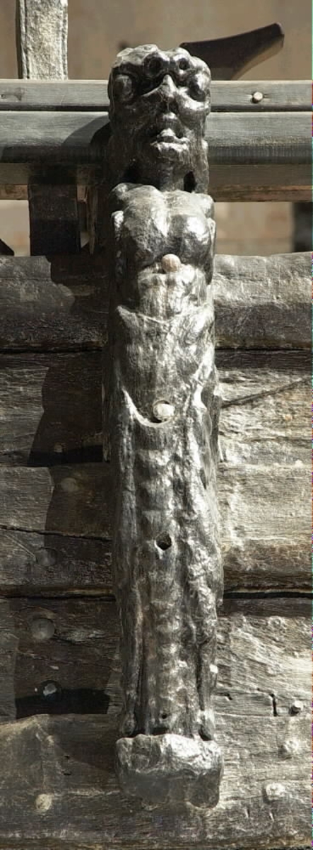Skulptur i form av en slätrakad herm med öppen mun och stor, bred näsa.
På hjässan sitter ett djurhuvud troligtvis föreställande ett lejon. Armar är ersatta av upprullade bladslingor. Hermens nederdel är formad till ett fodralliknande "hölje" prytt med bladslingor. Ornamentiken är av organisk karaktär med större och mindre, elegant formade bladslingor. Nedtill är "höljet" upprullat till en vulst. Sedd från sidan är hermen avsmalnande nedtill.
Baksidan, som har utgjort anliggningsyta, är försedd med ett antal stora urtag i höjd med hermens hjässa, bröstparti samt från midjan och nedåt. I midjehöjd återfinns även ett högsmalt urtag utmed baksidans ena hälft. Strax nedanför midjan går sidledes ett stort hål tvärs igenom skulpturen.
Skulpturen är delvis kraftigt sliten och finare detaljer i utförande har därför gått förlorade.

Text in English: Sculpture in the form of a clean-shaven Herm with open mouth and large, broad nose.
On top of his head is the head of an animal, possibly a lion. The arms have been replaced by strands of rolled-up leaves. The lower part of the Herm is sheathed in a "cover", decorated with leaf strands. The bottom of the "cover" is rolled up into a torus. Its ornamentation is of a pronounced organic character, with larger and smaller chains or festoons of leaves. Seen in profile, the Herm tapers downwards.
The back, also the attachment surface, has a number of large cut-out holes on the same level as the Herm''s head, chest, waist and further down. At one side of the back of the waist there is also a narrow vertical groove. Just below the waist, a large hole passes through the Herm.
The sculpture is very worn in places and any finer details have been lost.