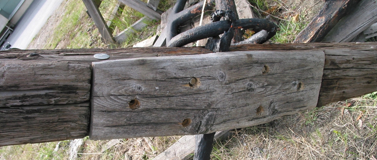 Ankarstock bestående av ett trästycke med urtag mitt på. Ankaret sitter i urtaget och hålls på plats med en modern träplatta.