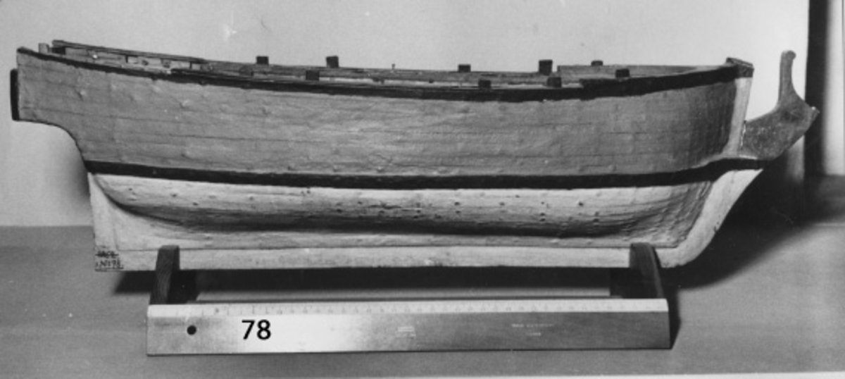 Skrovmodell av fartyg från 1700-talet, grovt tillverkad. Utförd med spant, bordläggning, garnering och uppbyggd galjon, men utan däck och rigg. Akterspegeln sönderbruten. Gulmålad på friborden, vattenlinjen och relingen svart, vit i botten, galjonen brun och insidan av relingen en röd rand.