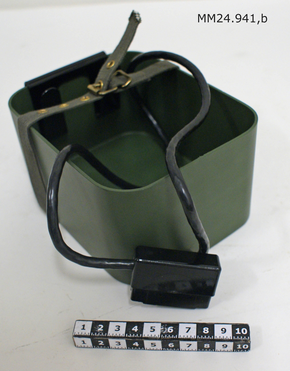 Rektangulär öppen kub av grön lättmetall. Inuti lådan sitter en svart förlängningskabel med kontaktdon. Runt lådan sitter en kanvasrem.
