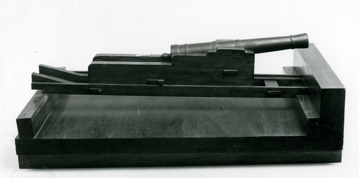Kanonmodell, 18-pundig kanonad i lavettage, föreställande kursörlavett från engelska fregatten LATONA omkring 1800. Kannen av svartmålat trä. Kursör av ek med blybeslag. Rattarna saknas. Fernissad.