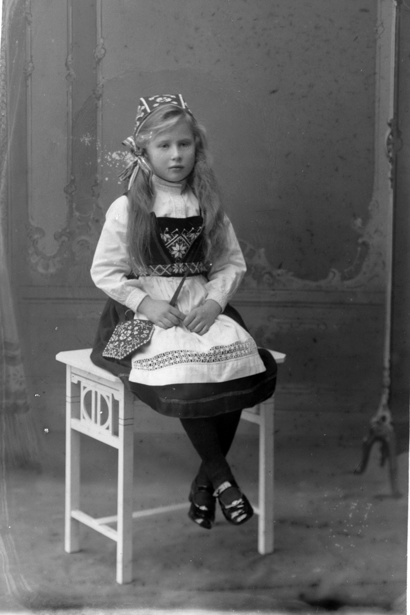 Studioportrett i helfigur av en sittende Eva Kulseng-Hansen i bunad.