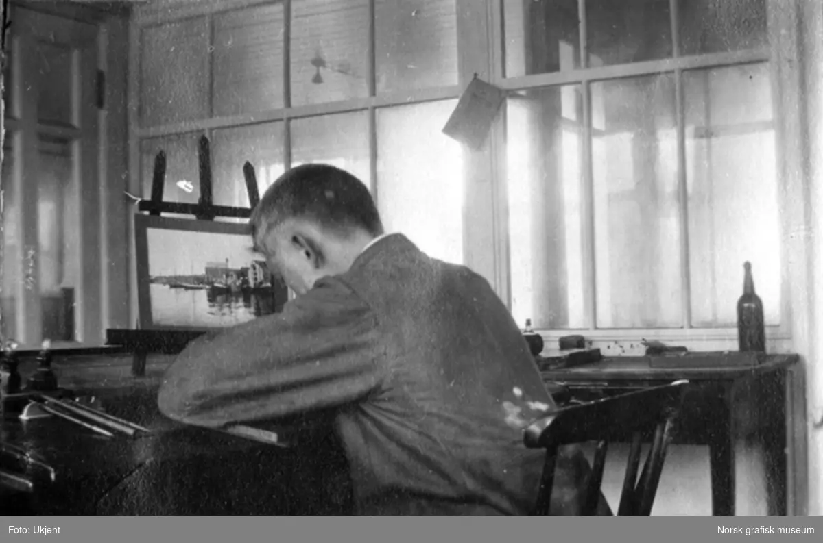Mann sitter ved arbeidspult med ryggen til fotografen.
Albumtekst:
"Et av T.s sjeldne øyeblikk (han arbeider)." 1917