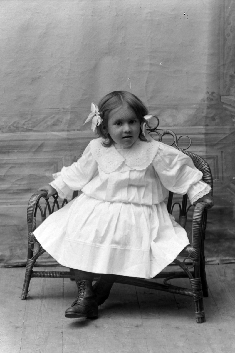 Studioportrett av liten jente i stol.
