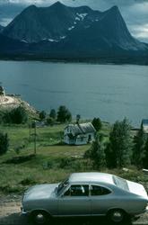 Hus i en bakke ned mot sjøen. I bakgrunnen fjord og fjell, i