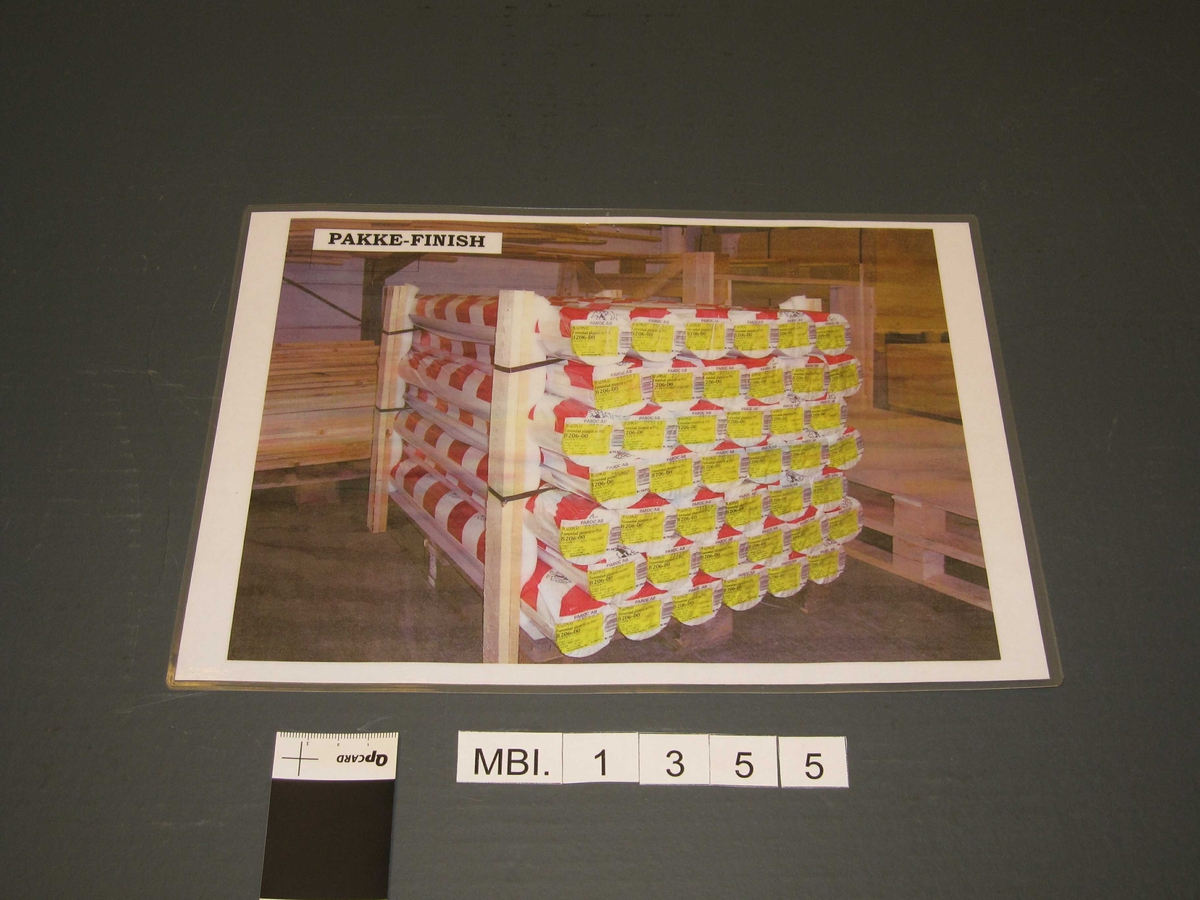 Plakaten viser en pall i lagerlokale stablet med 42 innpakkede ruller krøllfolie.  