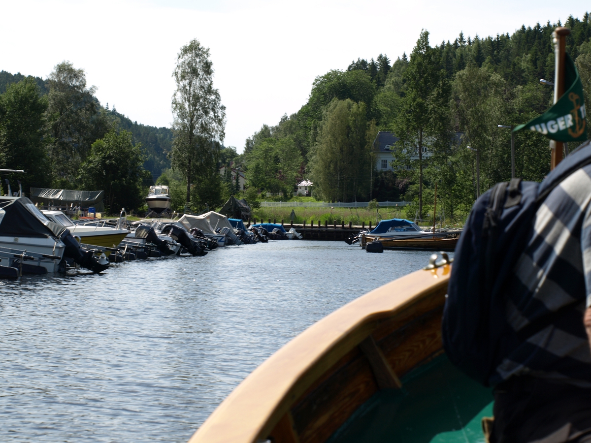 Fra sjøveien ser man inn mot Møla med mange brygger og småbåter. Sørover ligger en bondegård og et nyere boligfelt. Foto: Bodil Andersson, Østfoldmuseene/Halden historiske Samlinger.