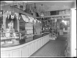 Interiør fra tekstilforretning  Ukjent sted.
Reklameskilt  