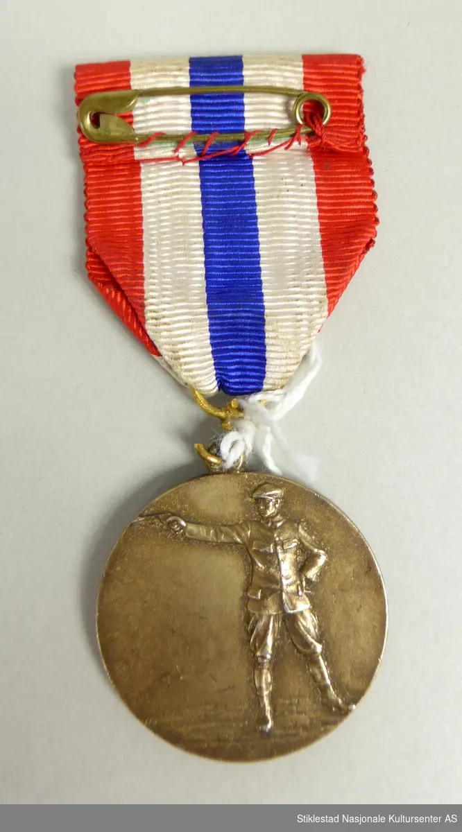 Medalje i messing med nasjonalfarget sløyfe/bånd. På forsiden er det en oval eikeløvskrans med inngravert tekst (MP- PIST. POLITIMESTERSKAP  GOTTRÔRA 1944). På baksiden en pistolskytter.