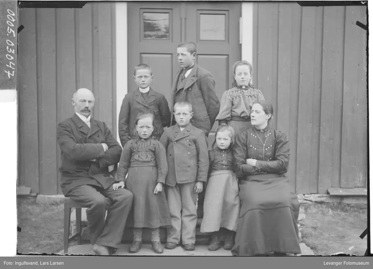 Gruppebilde av mann, kvinne og seks barn foran et inngangsparti.