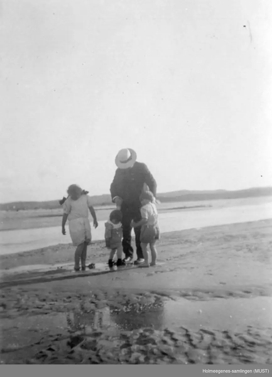 Tre barn og en voksen mann går tur langs en sandstrand.