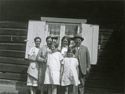 To kvinner, tre jenter og en mann står ved en husvegg. Rett 