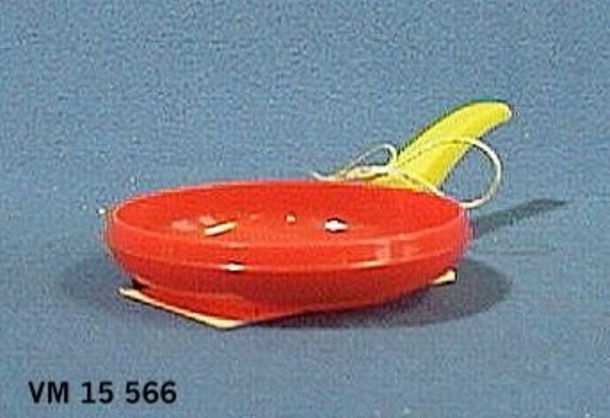 Stekpanna i röd plast med gult plasthandtag.