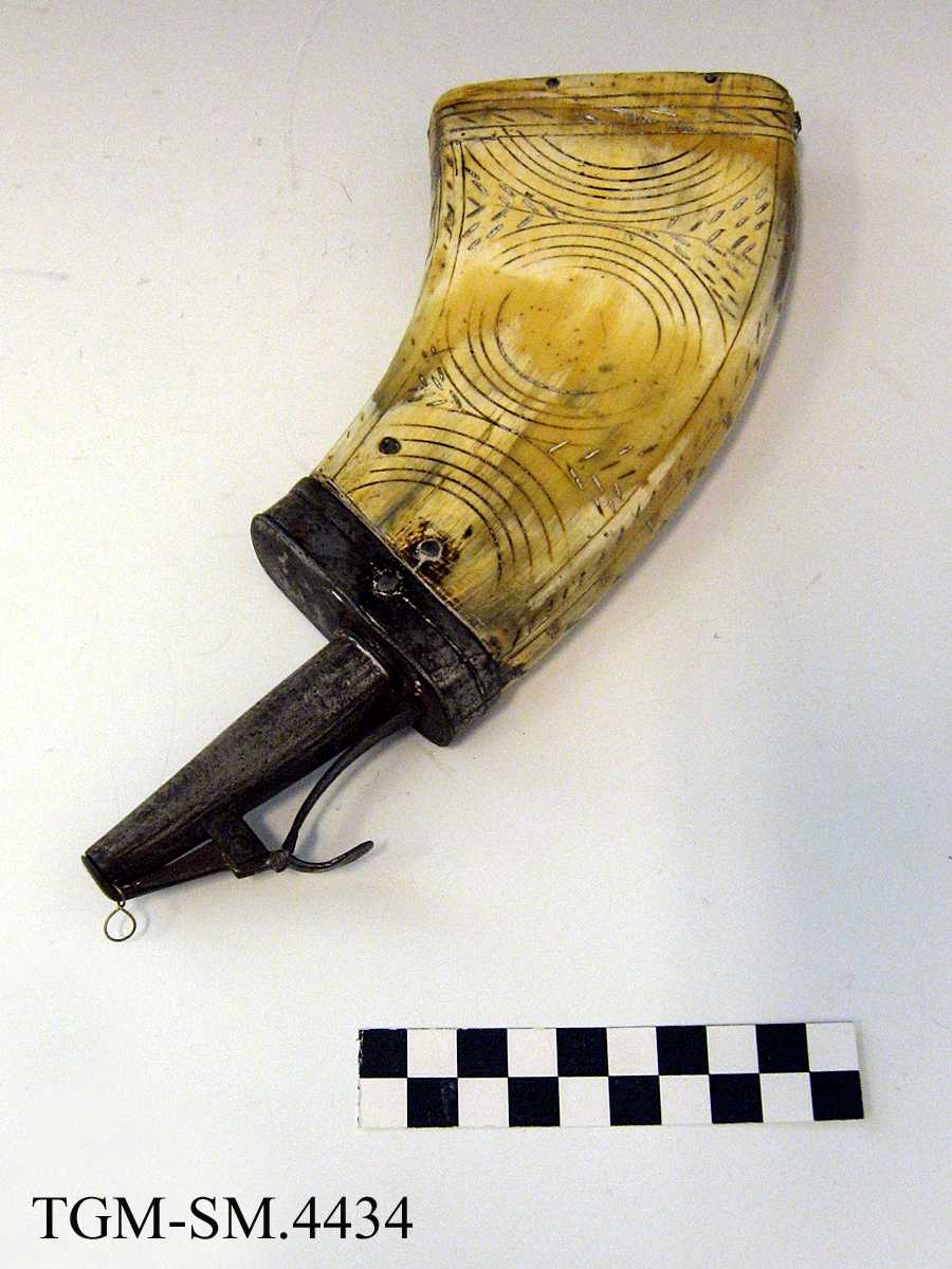 Fra protokollen: Fladt, med graverede billeder. Rimeligvis oksehorn presset fladt, firkantet. Træbund indfældt nederst, og ved den smalere ende jernbeslag med pipe som kan stænges og aapnes med en fjær. Aarstallet 1522 i det ene felt er muligens egte.
