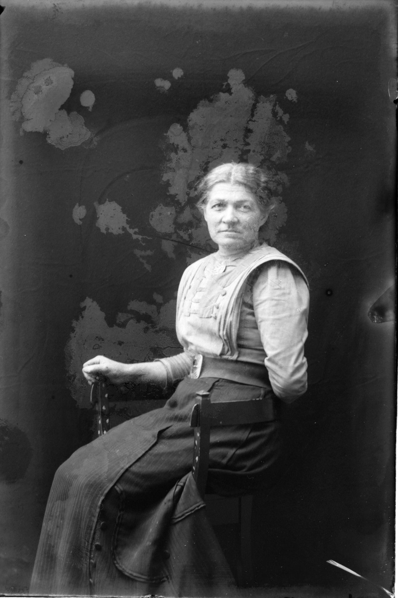Studioportrett av en eldre kvinne som sitter.