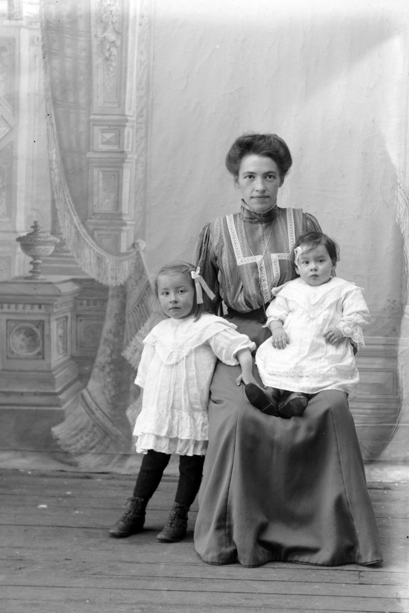 Studioportrett av en kvinne og to barn i helfigur.