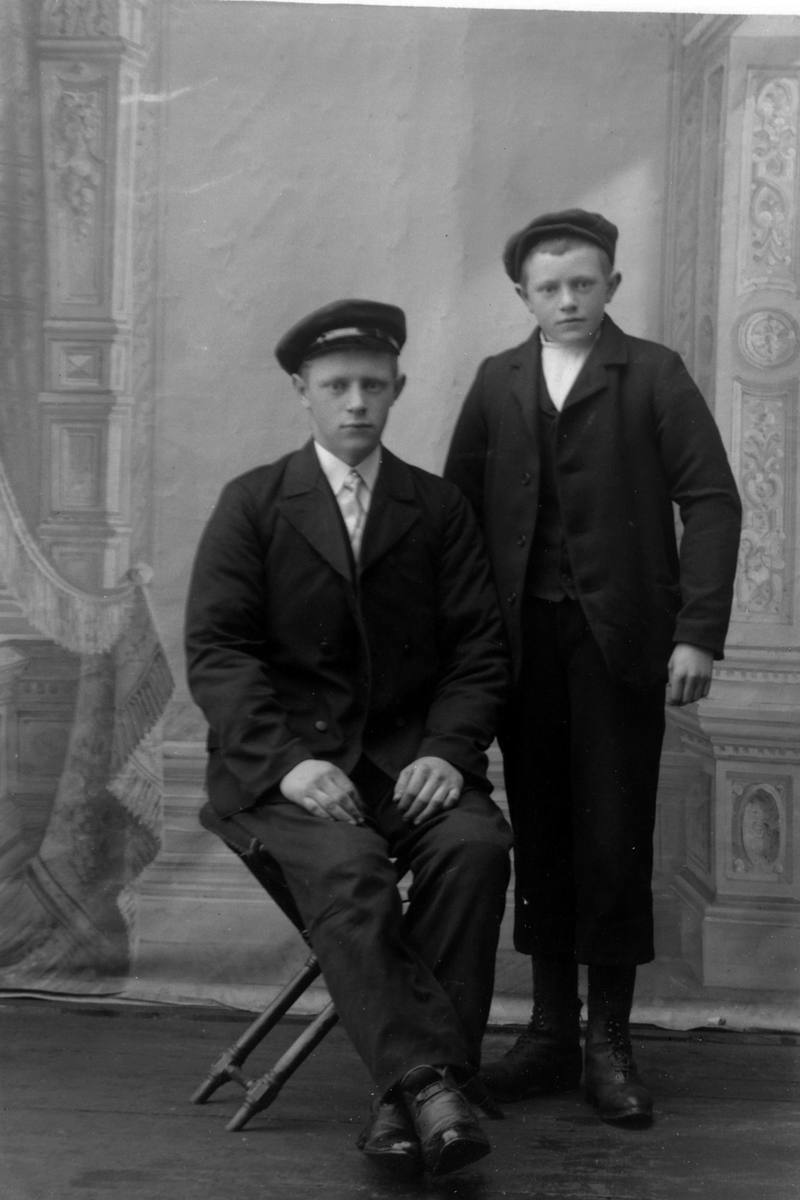Studioportrett av to unge menn med hatter på hodet.