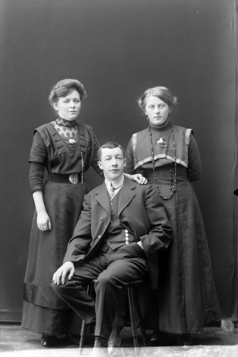 Studioportrett av en mann som sitter foran to stående kvinner.